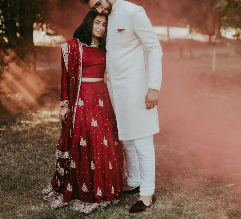 Bride & groom stand outdoors surrounded by orange smoke bomb