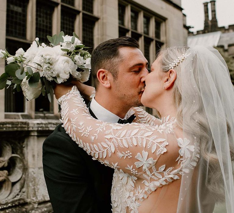 Bride wears floral wedding dress with lace embellishment and kisses her groom 