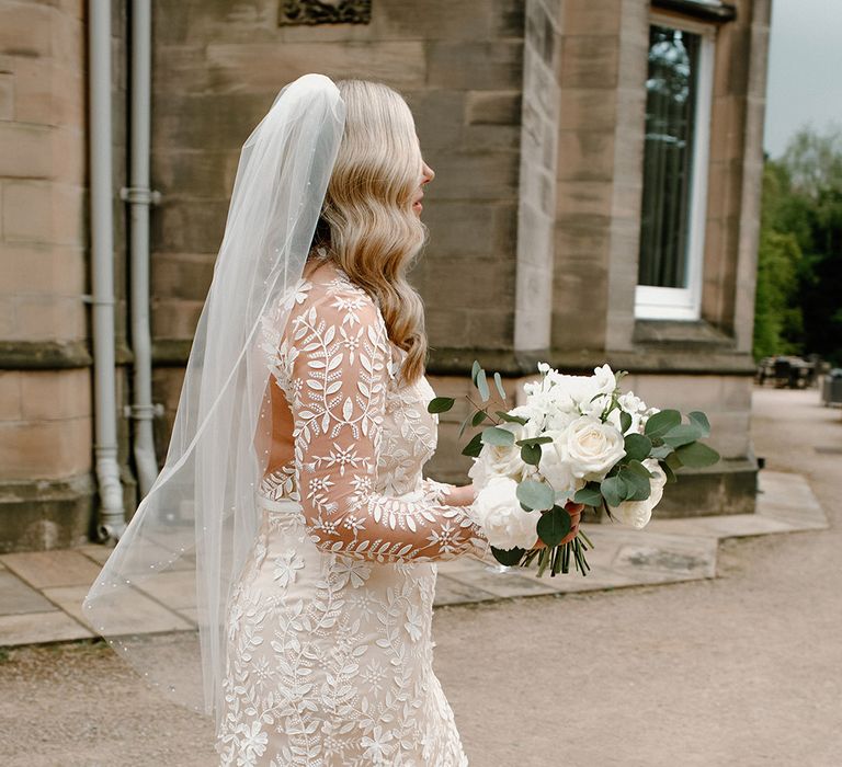 Bride wears backless long sleeve wedding dress with floral appliqué and cathedral veil 