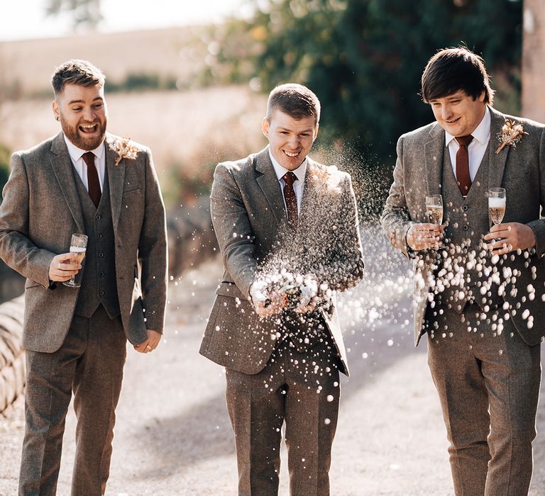 Champagne popping picture with groom and his groomsmen in three piece suits and burnt orange ties 