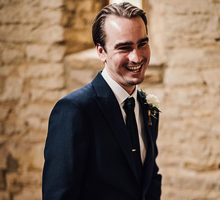 Smiling groom in a navy blue suit with a white rose buttonhole 