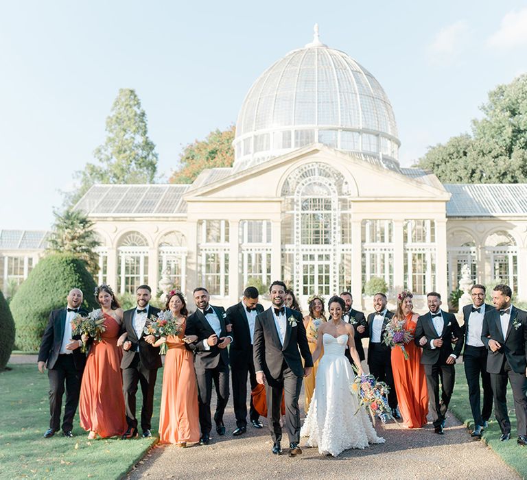 Bride & groom walk with their wedding party outside Syon Park Conservatory 