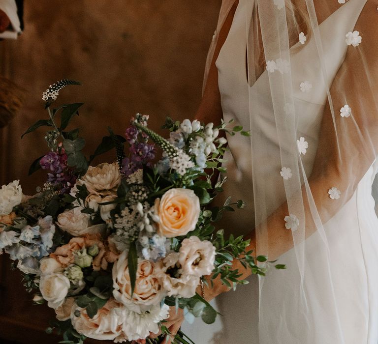 Bride holding a mixed floral bouquet with different colours in a Made With Love wedding dress and flower applique veil 