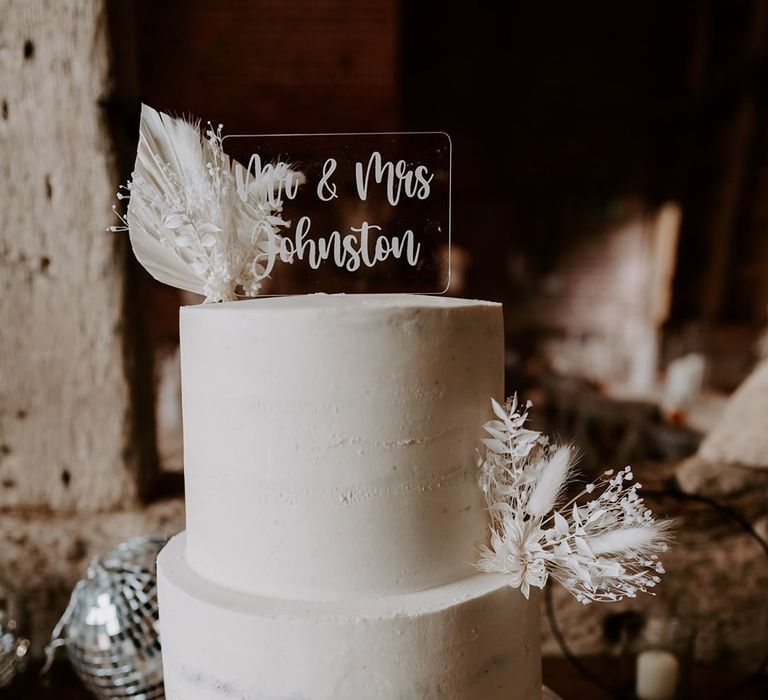 Two tier white frosted wedding cake with dried flower decor and personalised acrylic cake topper 