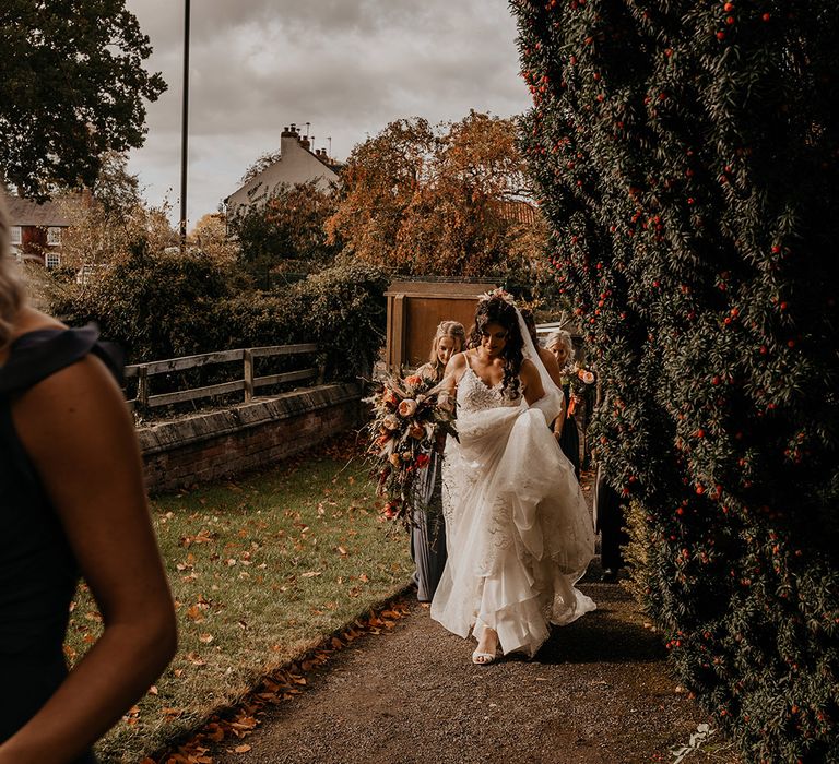 Bride holding a boho autumnal cascade wedding bouquet walking with her bridesmaids on the way to the church 