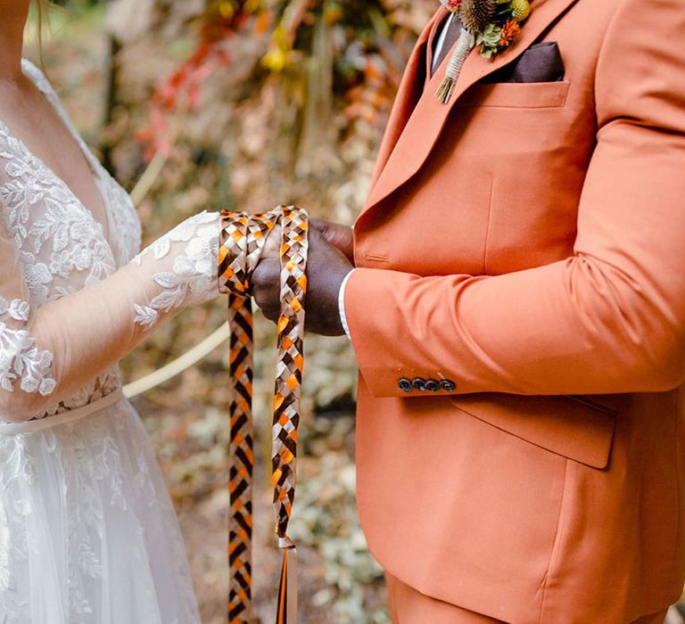 Bride and groom doing handfasting wedding ceremony at a harvest wedding with autumnal coloured handfasting ties 