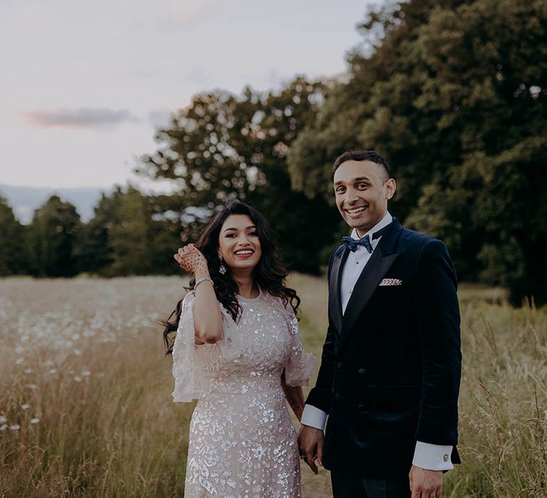 Bride wears embellished Needle & Thread reception dress beside her groom in blue velvet suit 