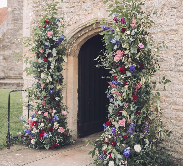 Wedding column flower arrangements with red, purple, and pink wedding flowers decorating the entrance to the church 