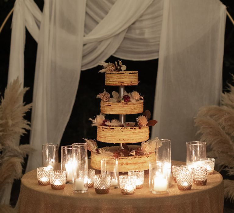 Opera wedding cake with floral decor surrounded by white pillar candles 