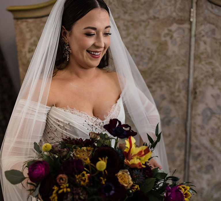 Bride in off the shoulder long sleeve tulle Wtoo by Watters wedding dress holding a purple and yellow spring wedding bouquet