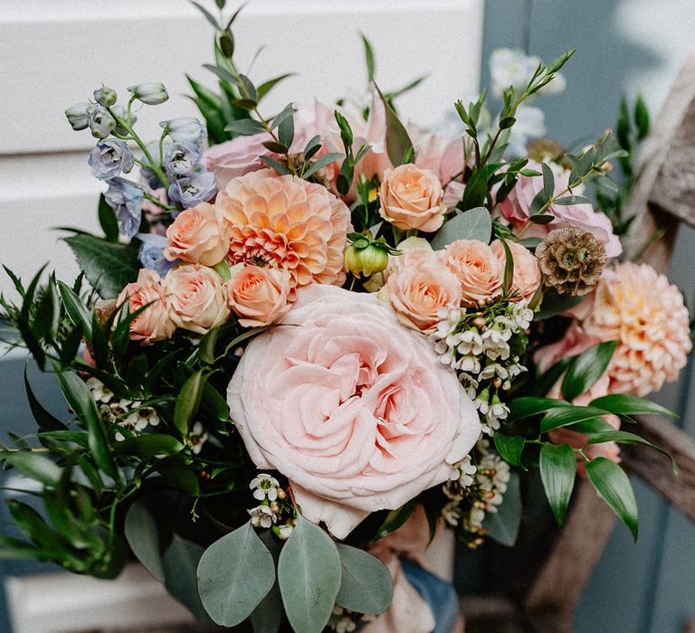 Spring wedding bouquet with blue, peach and pink wedding flowers including wax flower, roses and dahlias 