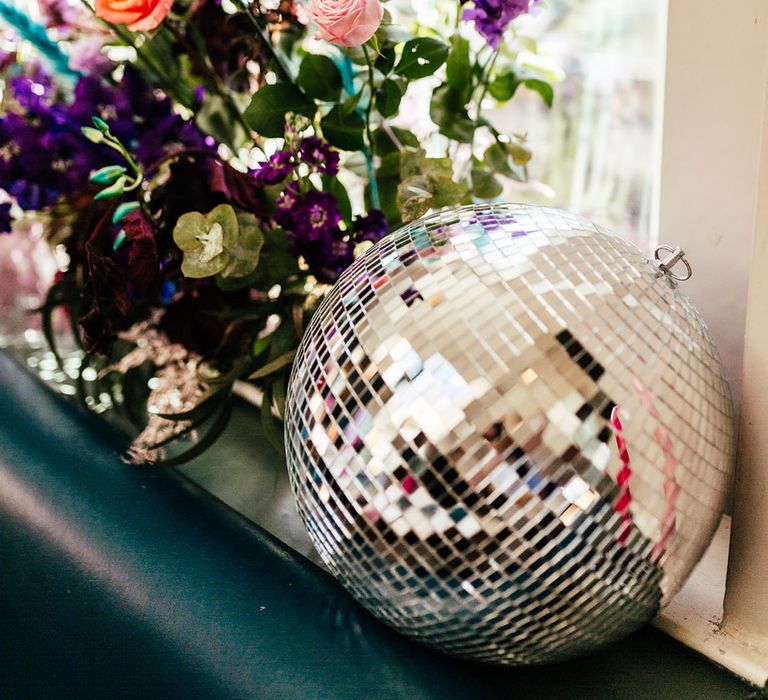 Large disco ball wedding decor next to pink garden roses, purple carnations, foliage and eucalyptus floral arrangement