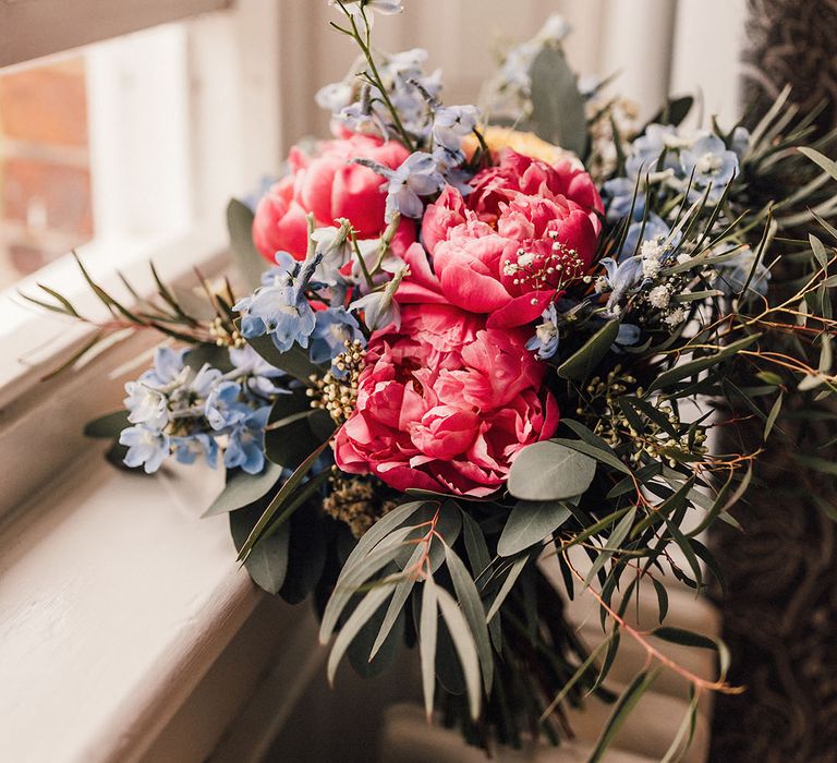 Bright pink peony bridal bouquet with small blue flowers and greenery for a greenery theme wedding 