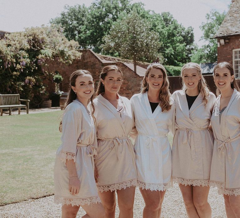 The bridesmaids wear pale pink robes with the bride in a white robe posing together as they get ready on the morning of the wedding 