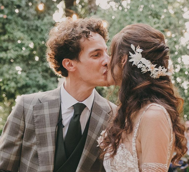 groom in a check suit kissing his bride in a gold sparkly wedding dress and dried flower hair accessory 