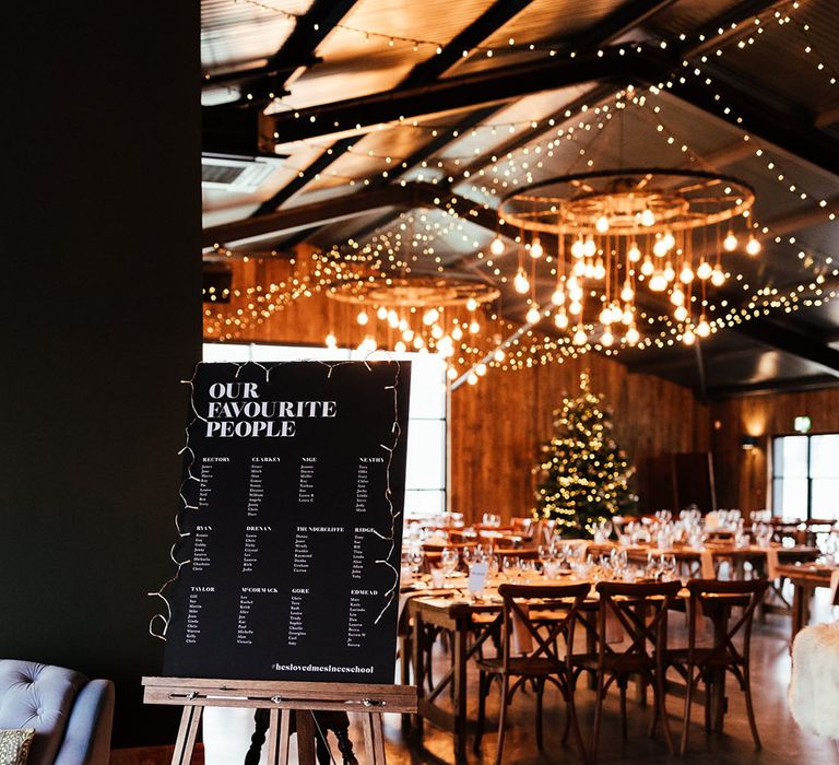 Cosy fairy lights, big festoon lights, and Christmas tree at Silchester Farm with black and white wedding table plan sign 