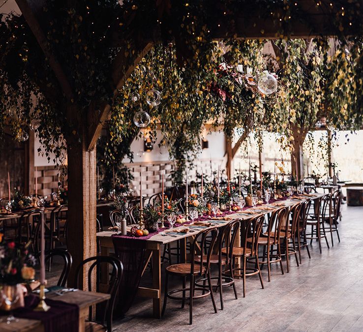 Cripps Barn wedding venue decorated with plenty of wild draping foliage with dark red and pink colour scheme full of taper candles 