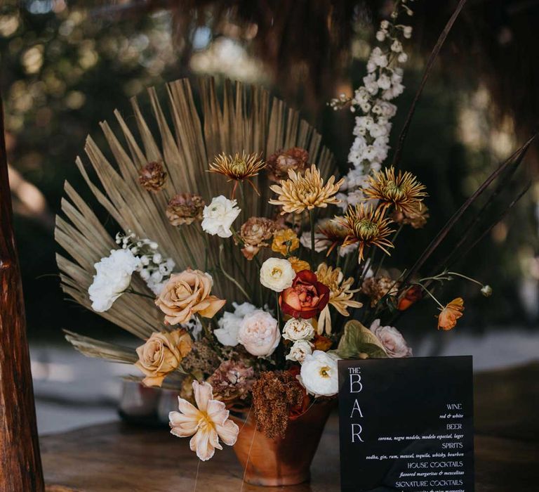 White, orange and burnt orange dried flower arrangements in ceramic vase with monochrome minimalistic bar sign 