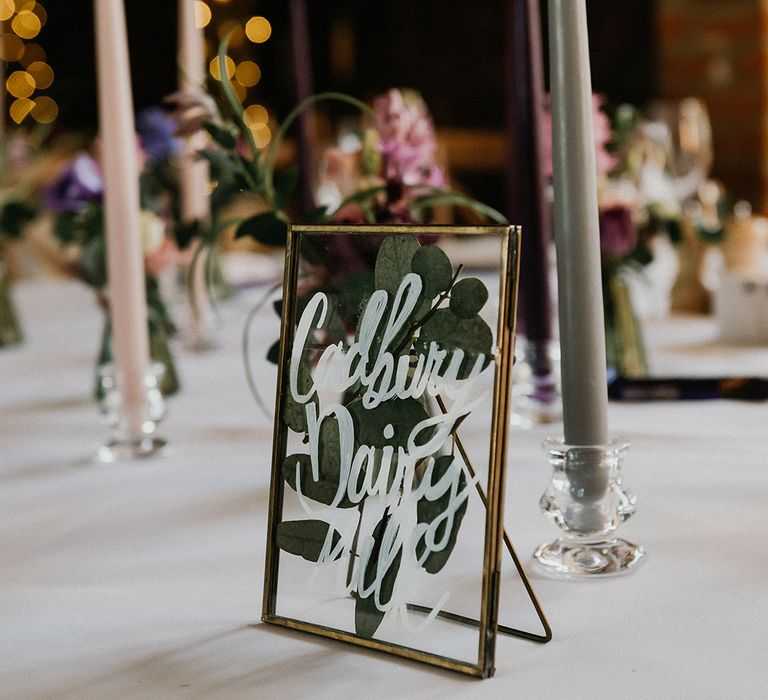 Grey and pink taper candles with gold photo frame with pressed leaves table name sign named after different chocolate bars 