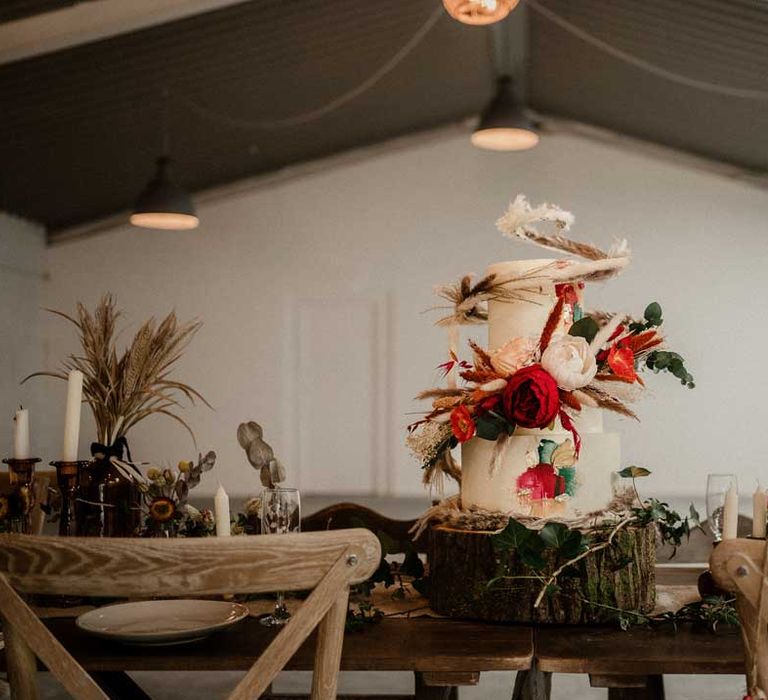 Three tier buttercream wedding cake with large decorative pampas grass, eucalyptus, dried flower and garden rose cake topper on large tree stump cake stand on boho rustic wedding tablescape at The Barn at Avington 