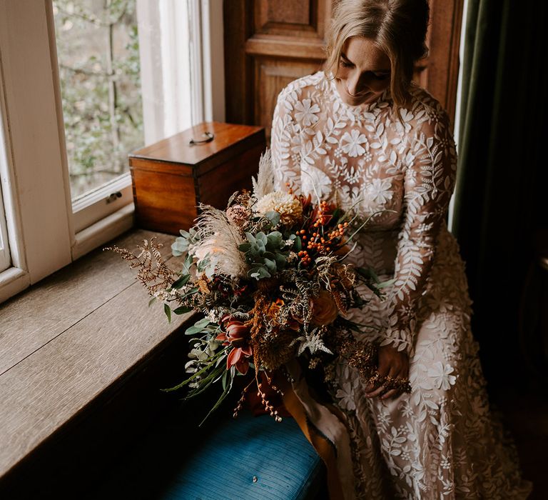 Bride in Catherine Deane boho lace wedding dress with long sleeves carrying and autumnal wedding bouquet 