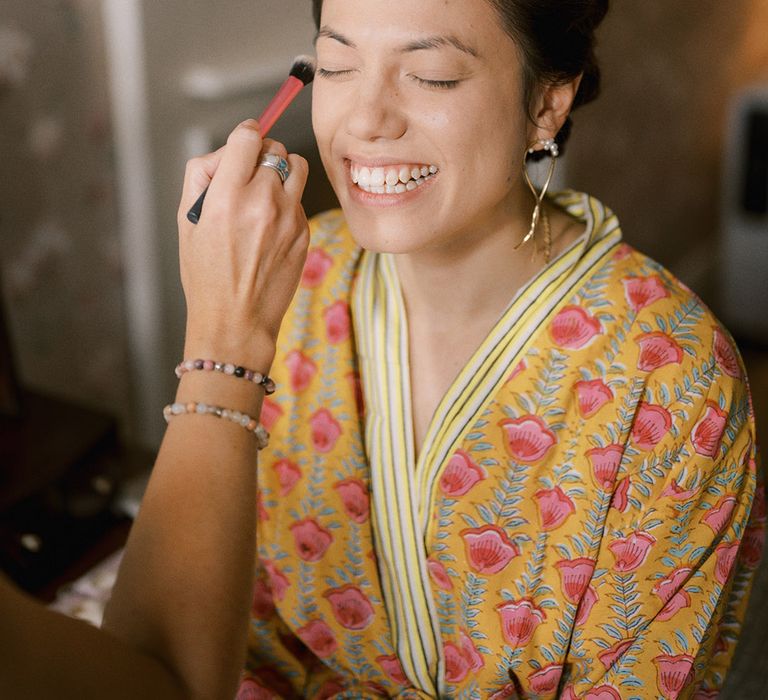 Bride wearing a colourful robe gets her makeup done for the wedding day 