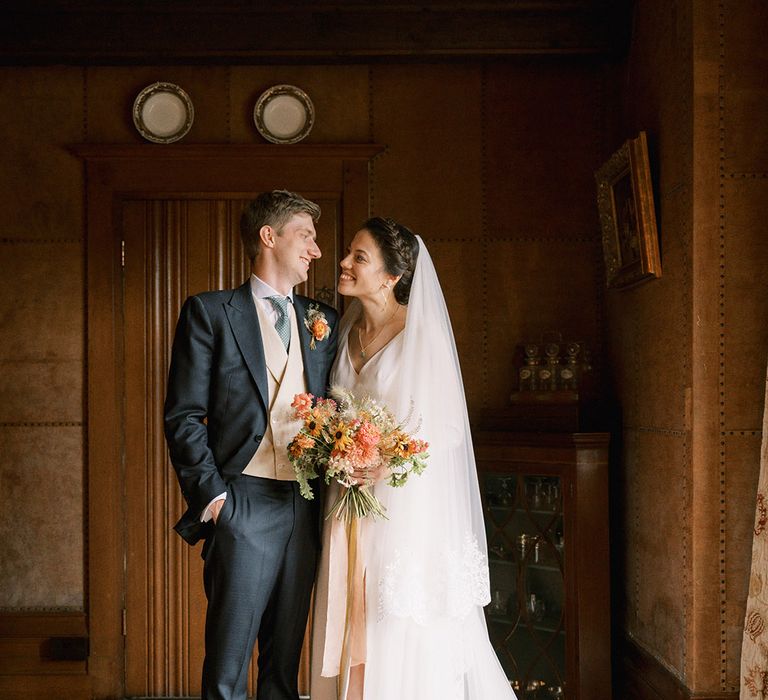 Bride in long sleeve traditional wedding dress by Andrea Hawke stating with groom in navy suit 