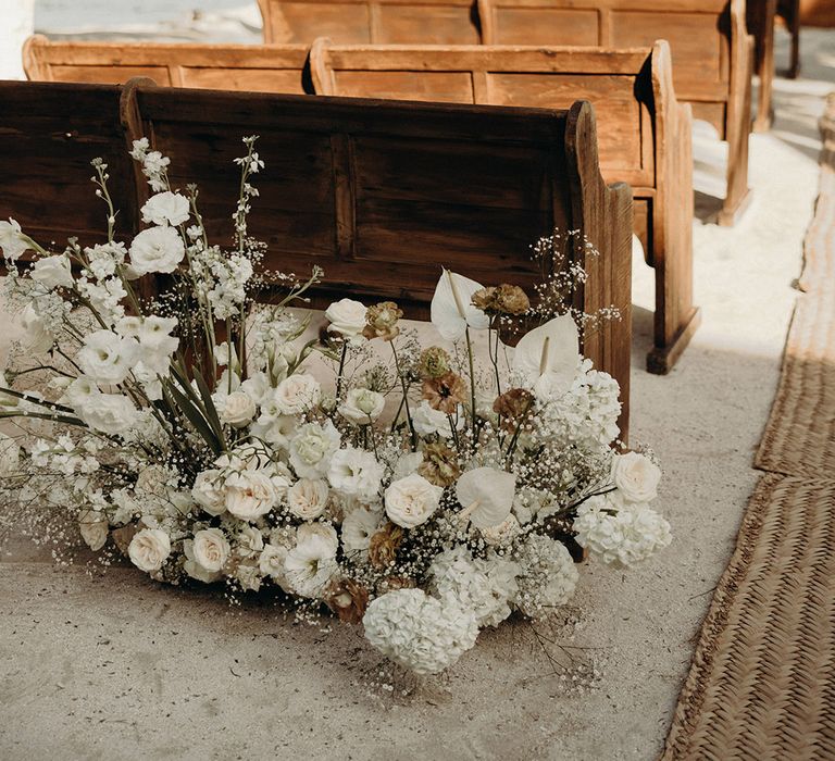 wooden church pews and white wedding flowers at beach wedding ceremony 