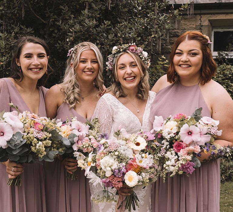 Bridal party in pink bridesmaid dresses with pastel bouquets with the bride wearing a wildflower wedding crown 