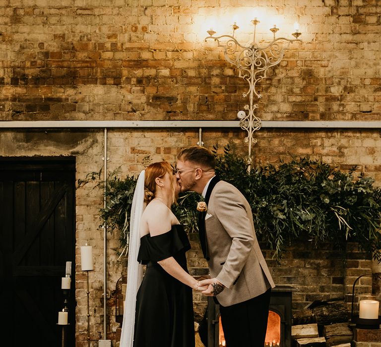 Bride in black satin bias off the shoulder wedding dress kissing the groom at their rustic wedding 