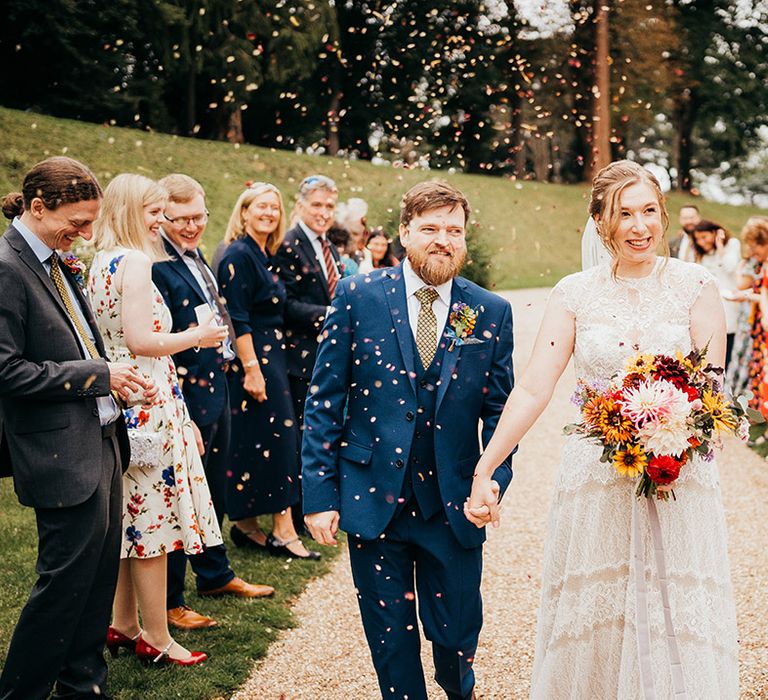 Groom in blue suit exits from the wedding ceremony with the bride in a lace wedding dress 