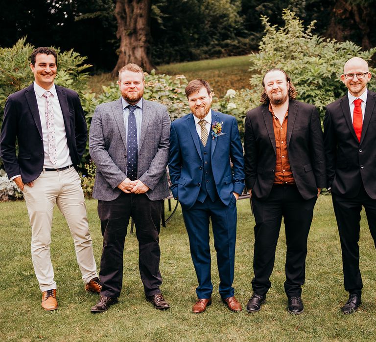 Groom and groomsmen standing together in mismatched wedding suits