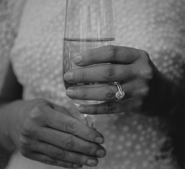 Bride holding a glass of champagne showing off her oval engagement ring and matching wedding band 