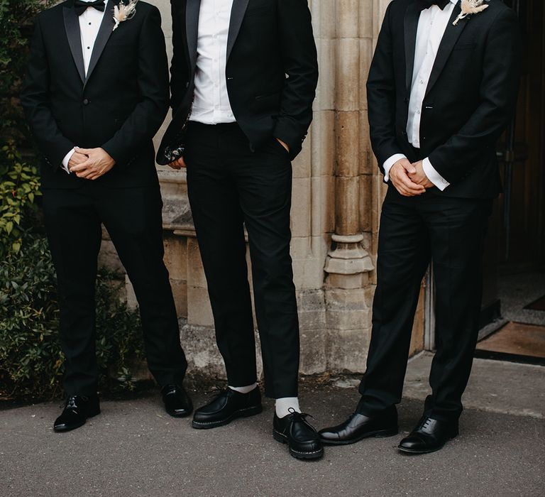 Groomsmen in black tuxedos wearing dried flower boho buttonholes 