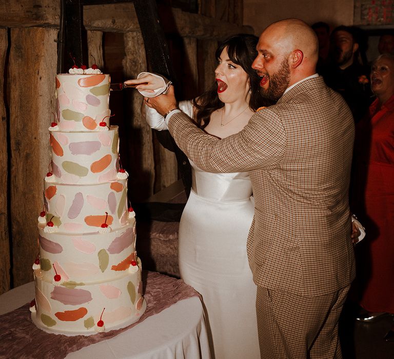 Bride and groom cut their five tier wedding cake with painted icing design 