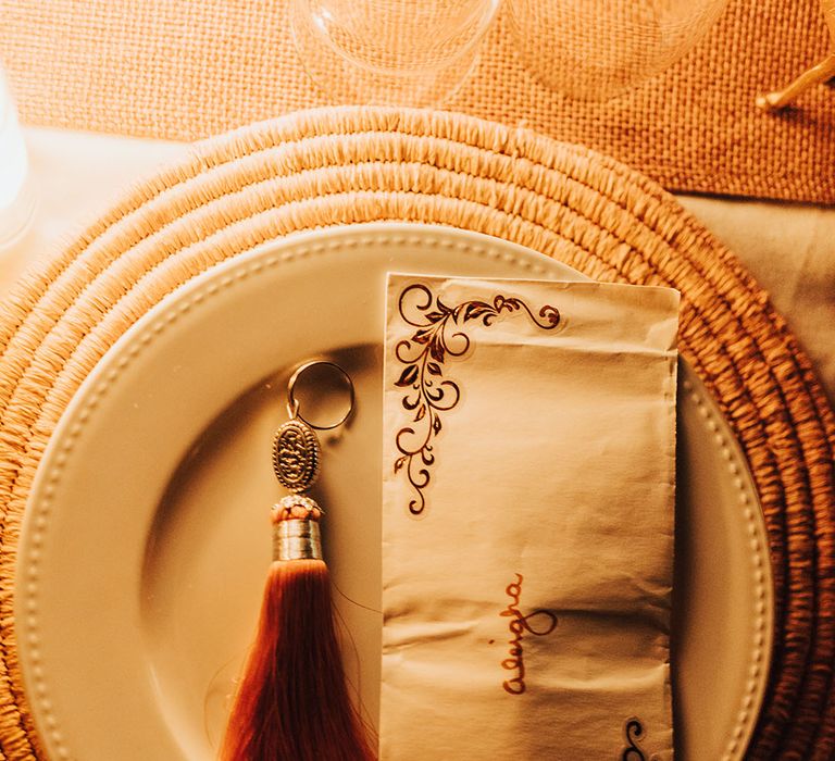 Wicker place mat and white plate with decorated napkin and place name 