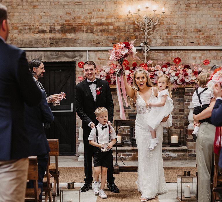 The bride and groom walking back down the aisle as a married couple with their children 