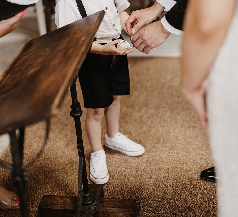 Little boy ring bearer in white shirt with black tie and braces giving the groom the wedding rings 