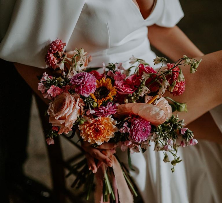 Bride holding pink and orange wedding bouquet with dahlias, roses and sunflowers 