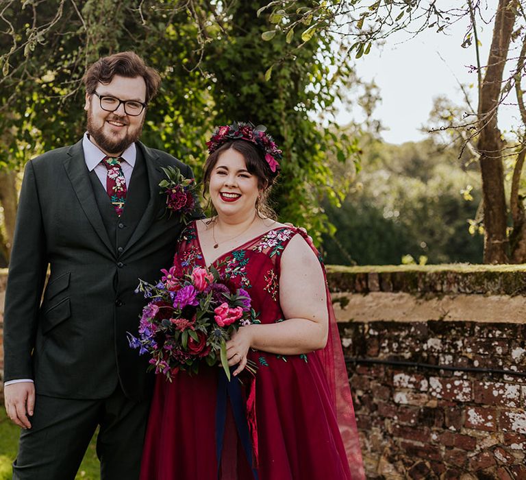 Groom in three piece green suit with bride in a deep red floral embroidered wedding dress 