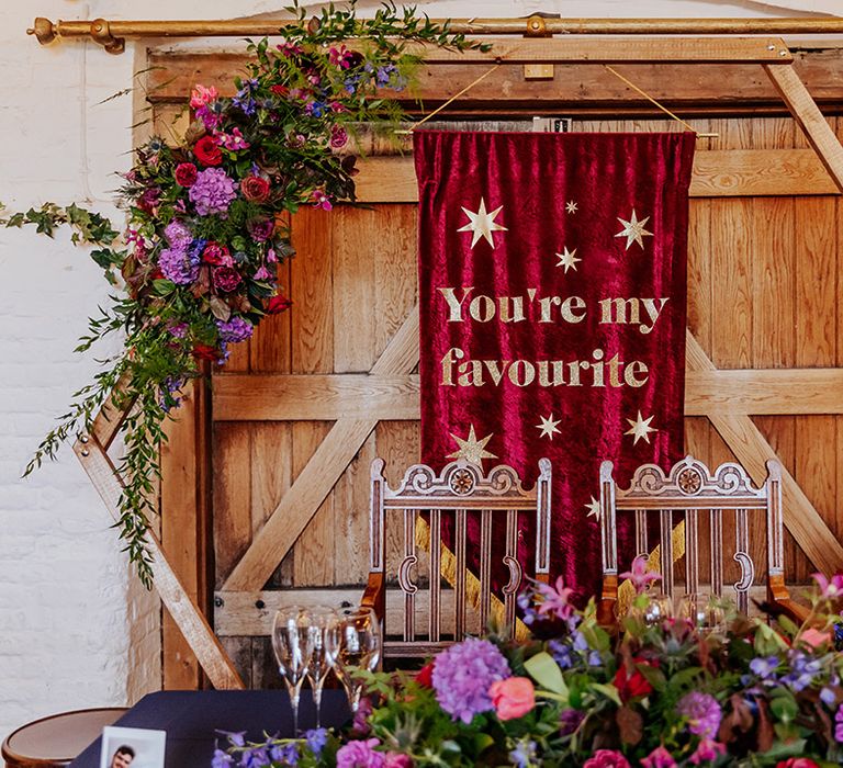 Dark red and gold wedding banner signage as backdrop to sweetheart table 