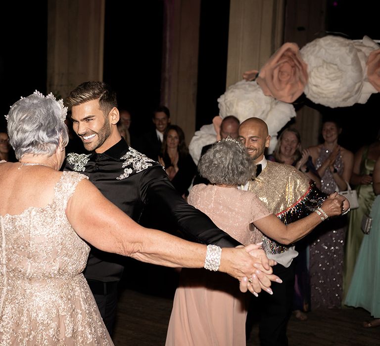 The two grooms dance with their mothers at their wedding reception in their sparkly wedding reception outfits 