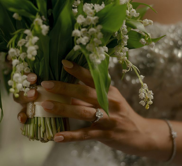 Bride wearing large cushion cut diamond engagement ring holding white flower bouquet 