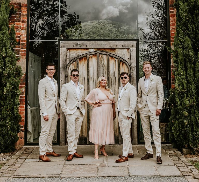 Groomsmen wearing neutral beige wedding suits with a groomswoman in pale pink bridesmaid dress 