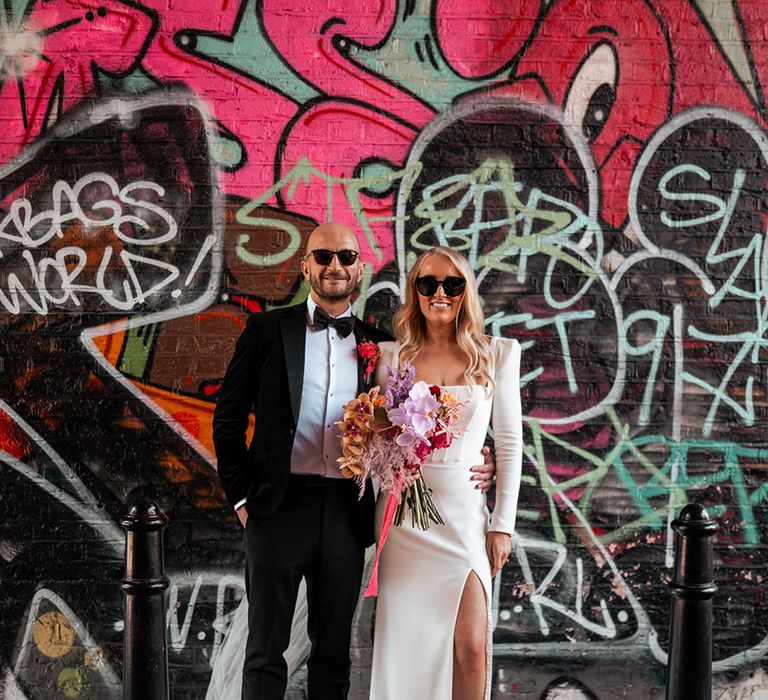 The bride and groom pose together outside urban graffiti backdrop at London wedding