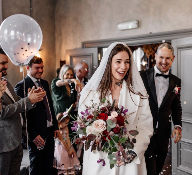 Bride in jumpsuit and polka dot veil entering the pub wedding reception 