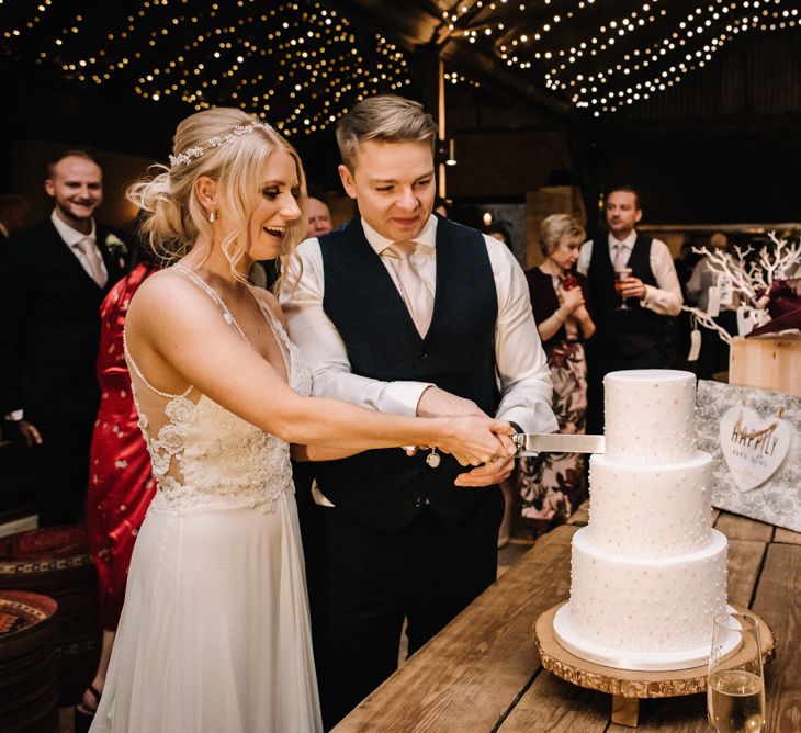 Bride and groom cutting classic white wedding cake with three tiers 