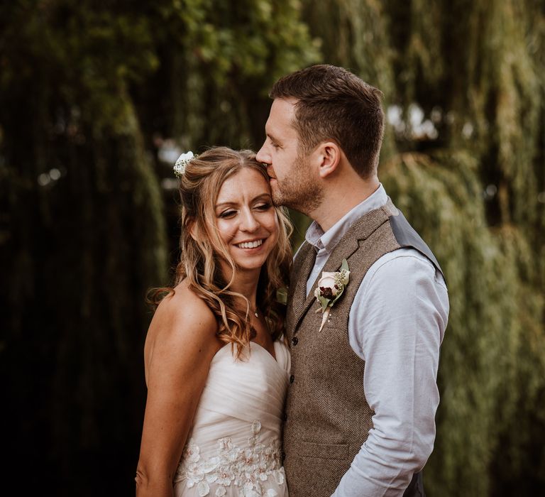 Groom in tweed waistcoat kissing his brides head 