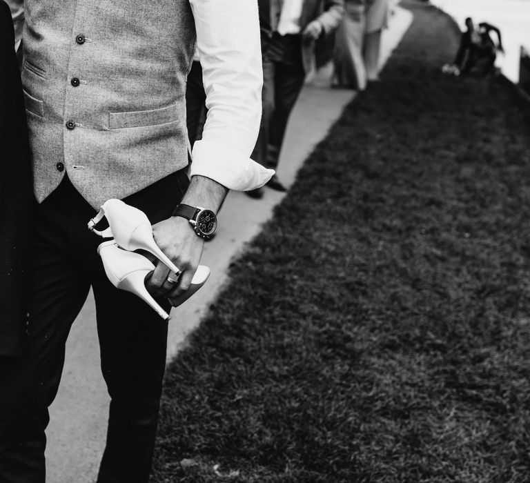 Groom holds brides shoes 