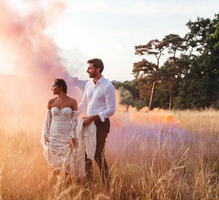 Bride & groom stand in field with colourful smoke bomb 